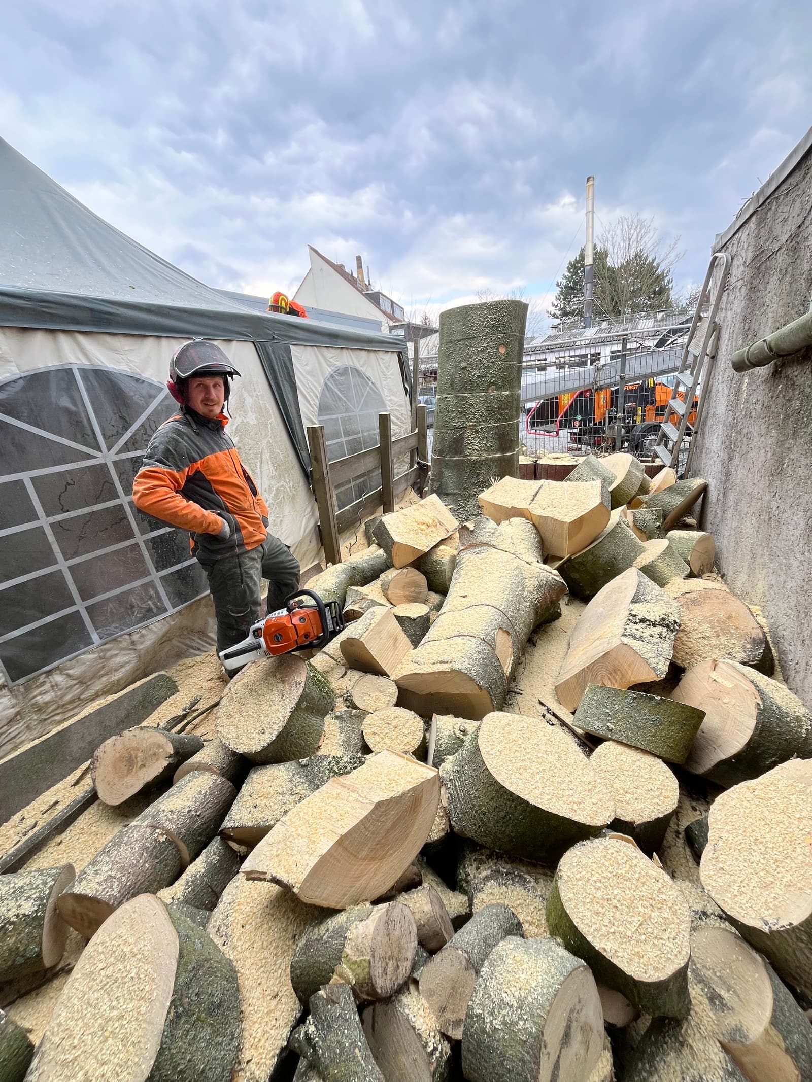 Jakob Mundhenke mit Kettensäge vor aufgearbeitetem Stammholz